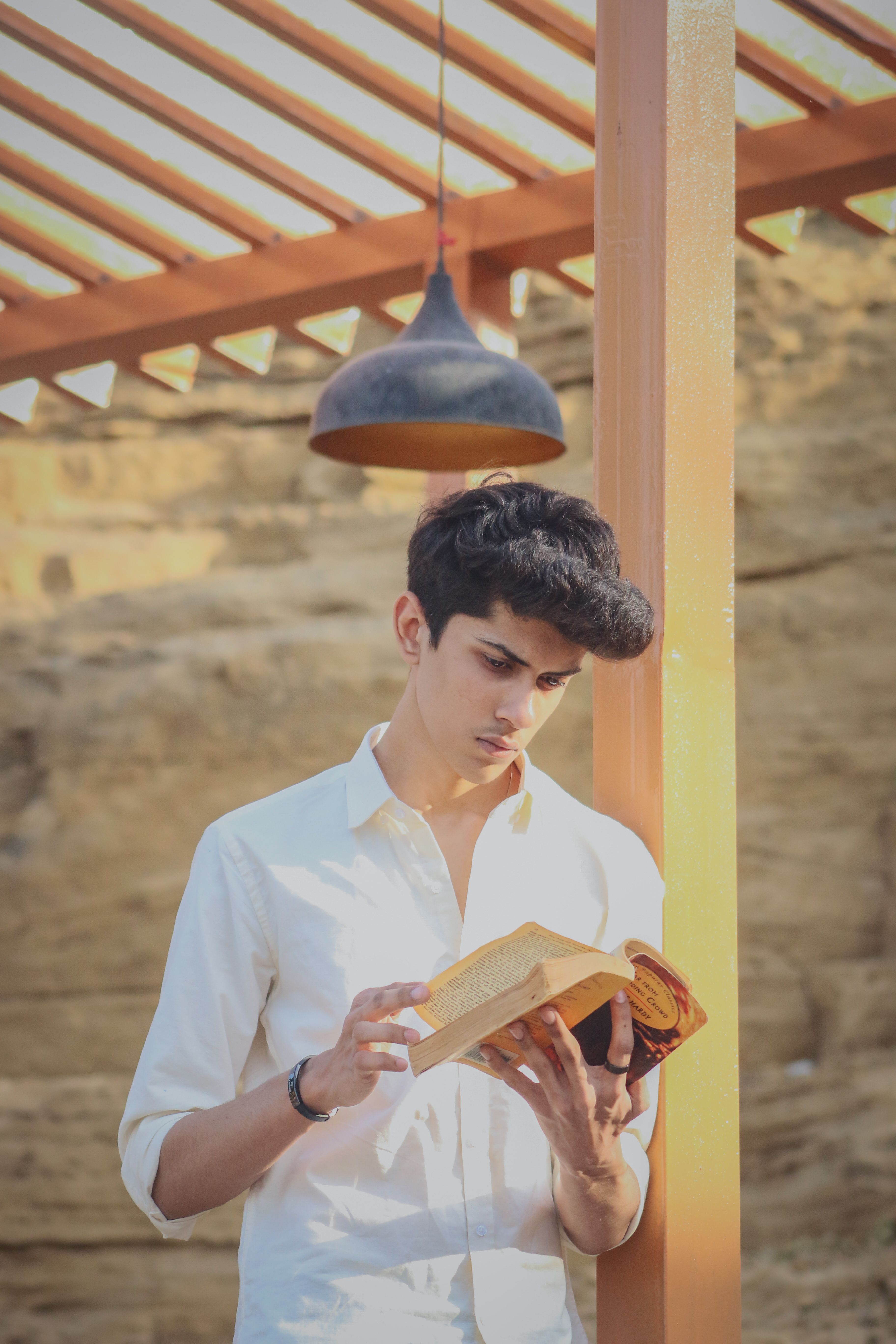 Young man reading a book outdoors under a wooden pergola. Bright sunny day