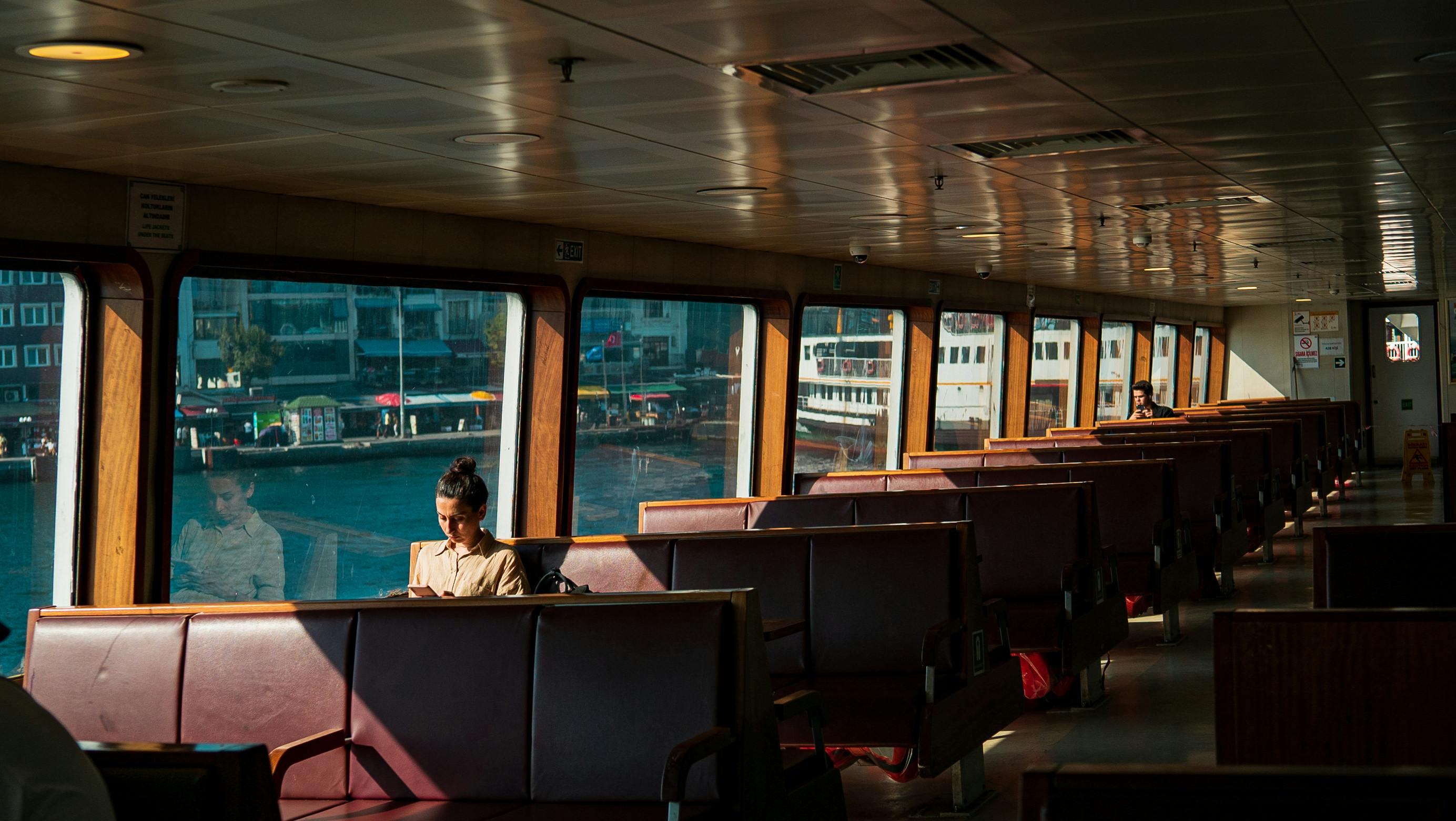 Passengers enjoy a peaceful journey on a sunlit ferry with large windows.