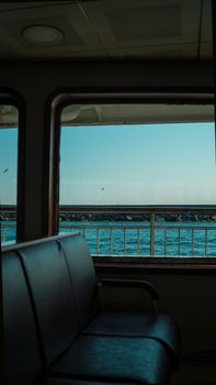 View of the sea through a ferry window with empty seats inside, creating a calm travel vibe.