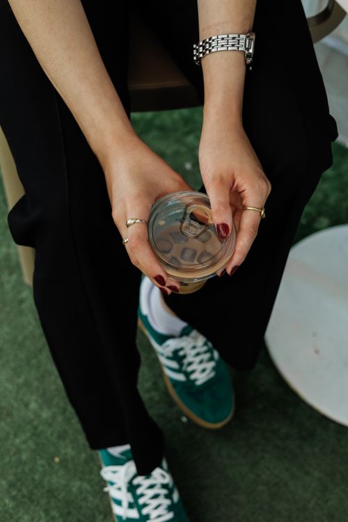 Free A stylish woman holding a fresh iced drink, captured from above, showcasing casual fashion and a refreshing moment. Stock Photo