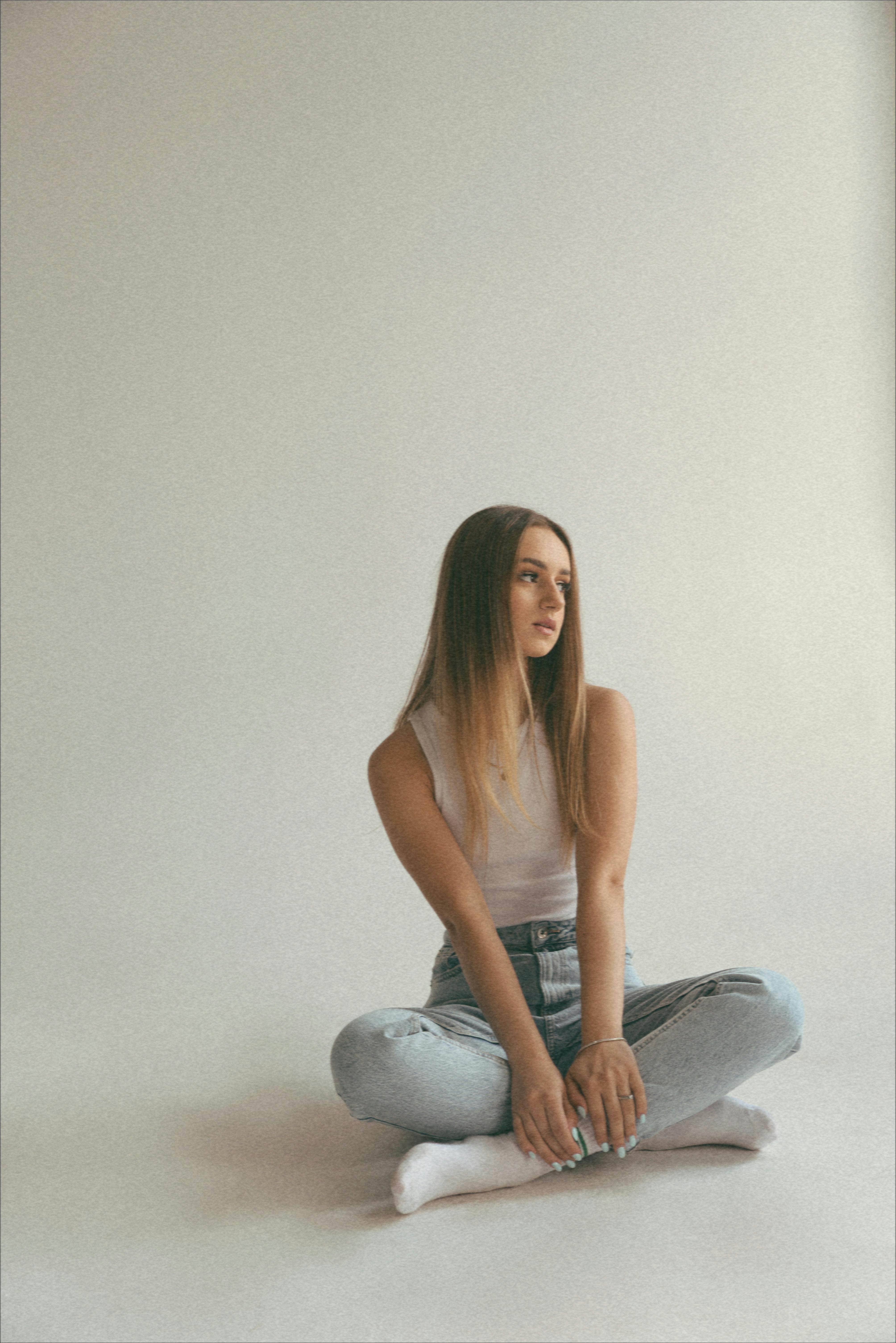 Young woman in a relaxed pose wearing casual clothing, sitting on the floor indoors.