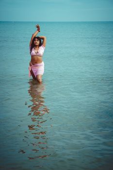 A woman in pink swimwear enjoys a sunny day at the beach, standing in turquoise water.