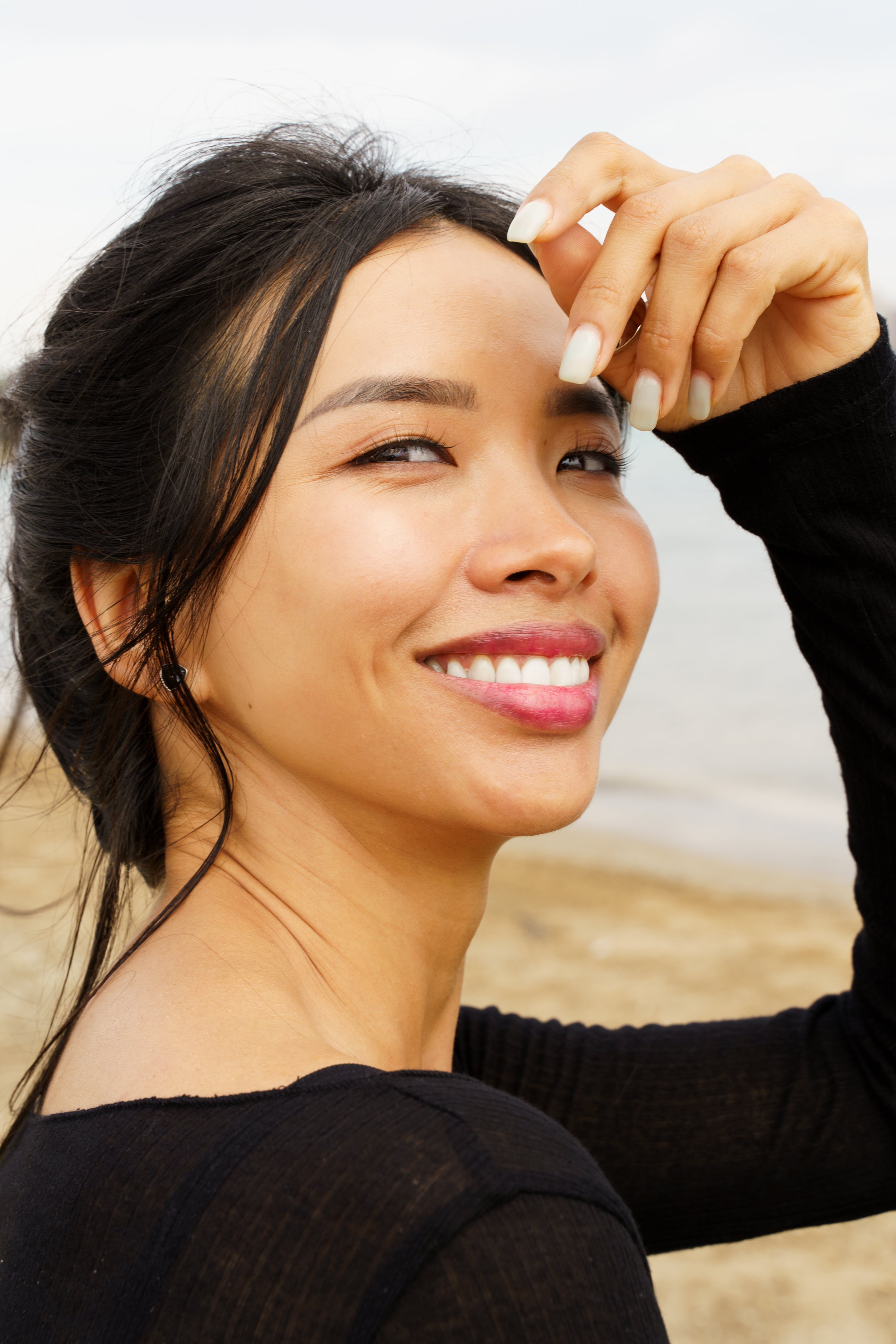A young woman smiles warmly against a sandy beach backdrop, exuding a relaxed and joyful vibe.