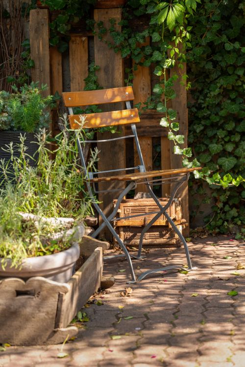 Free A cozy garden patio with a wooden folding chair surrounded by lush greenery and plants. Stock Photo
