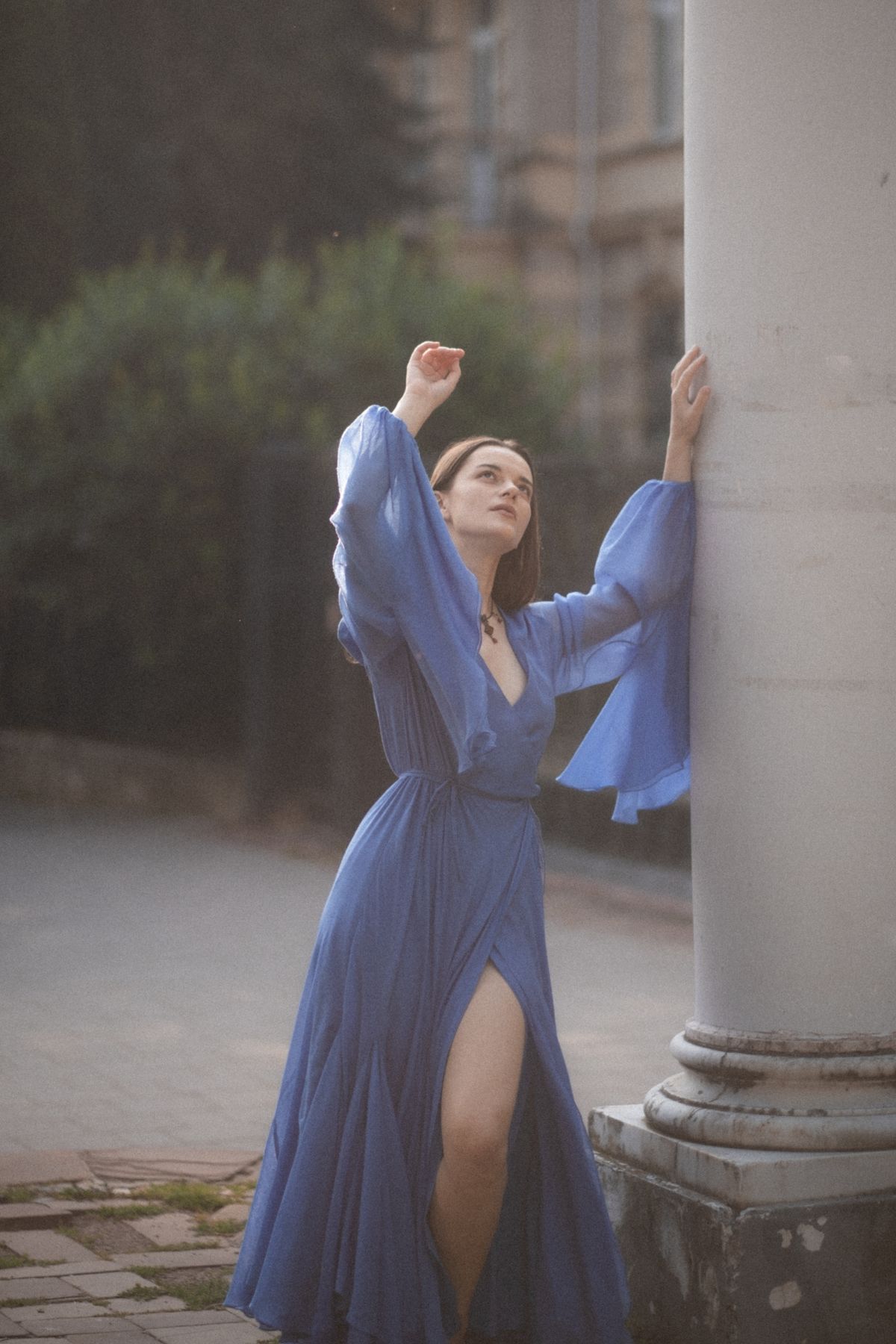 A woman in a blue chiffon dress leaning against a pillar