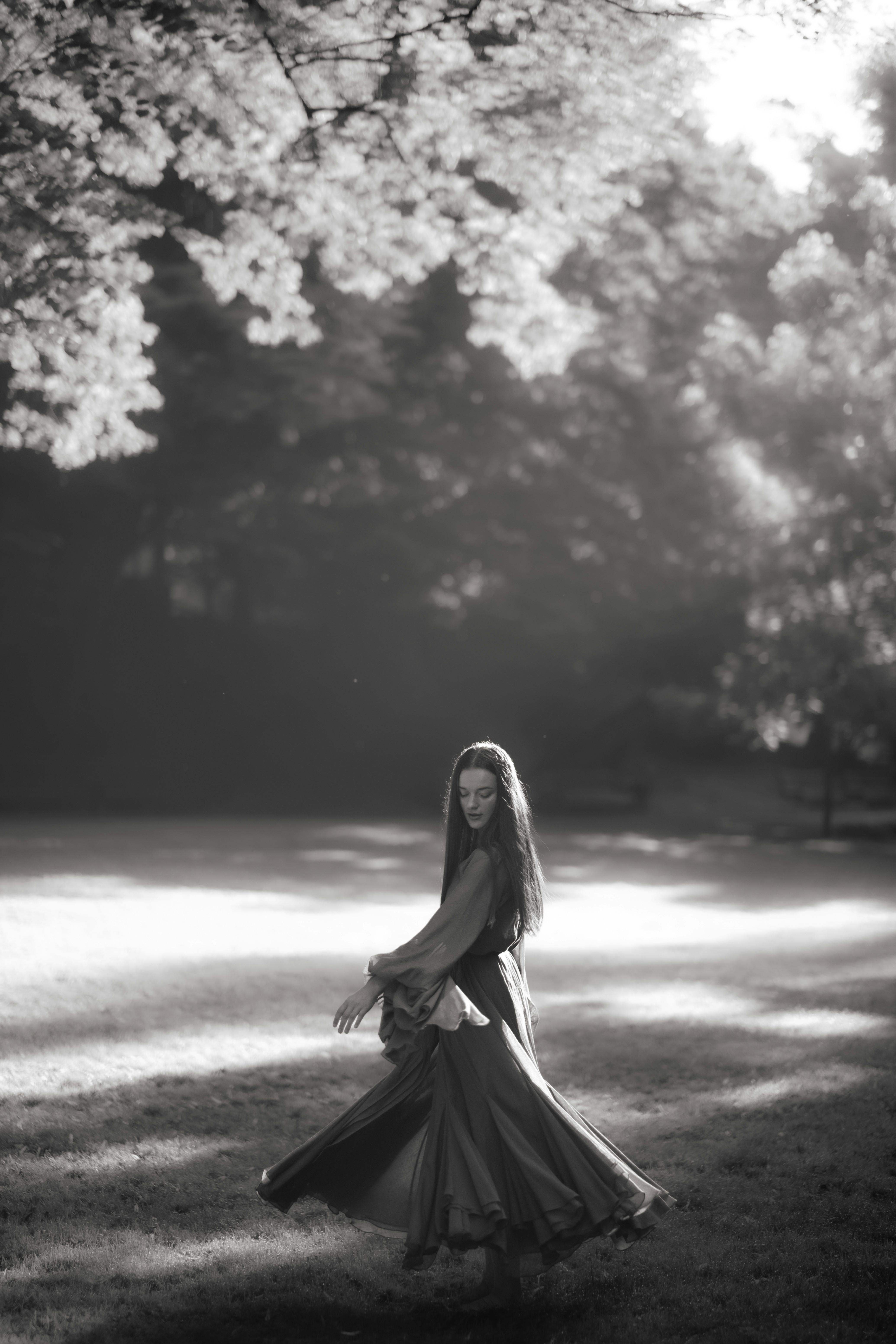 Elegant black and white portrait of a woman twirling gracefully in a sun-dappled outdoor setting.