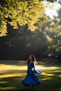 A serene image of a woman twirling in a blue dress amidst a sunlit park setting.