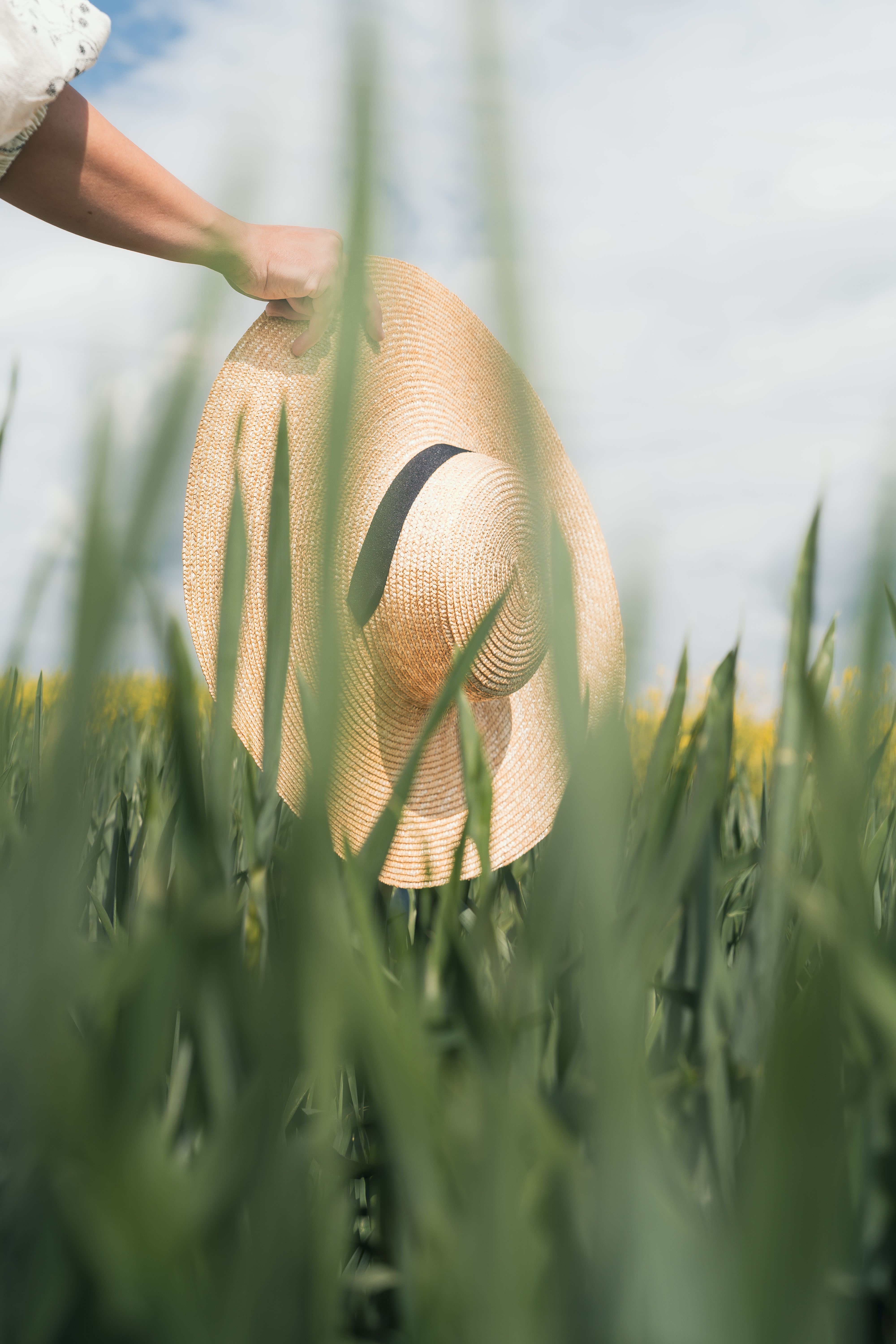 A woman holding a straw hat in a lush green field under a blue sky. Perfect for seasonal imagery.