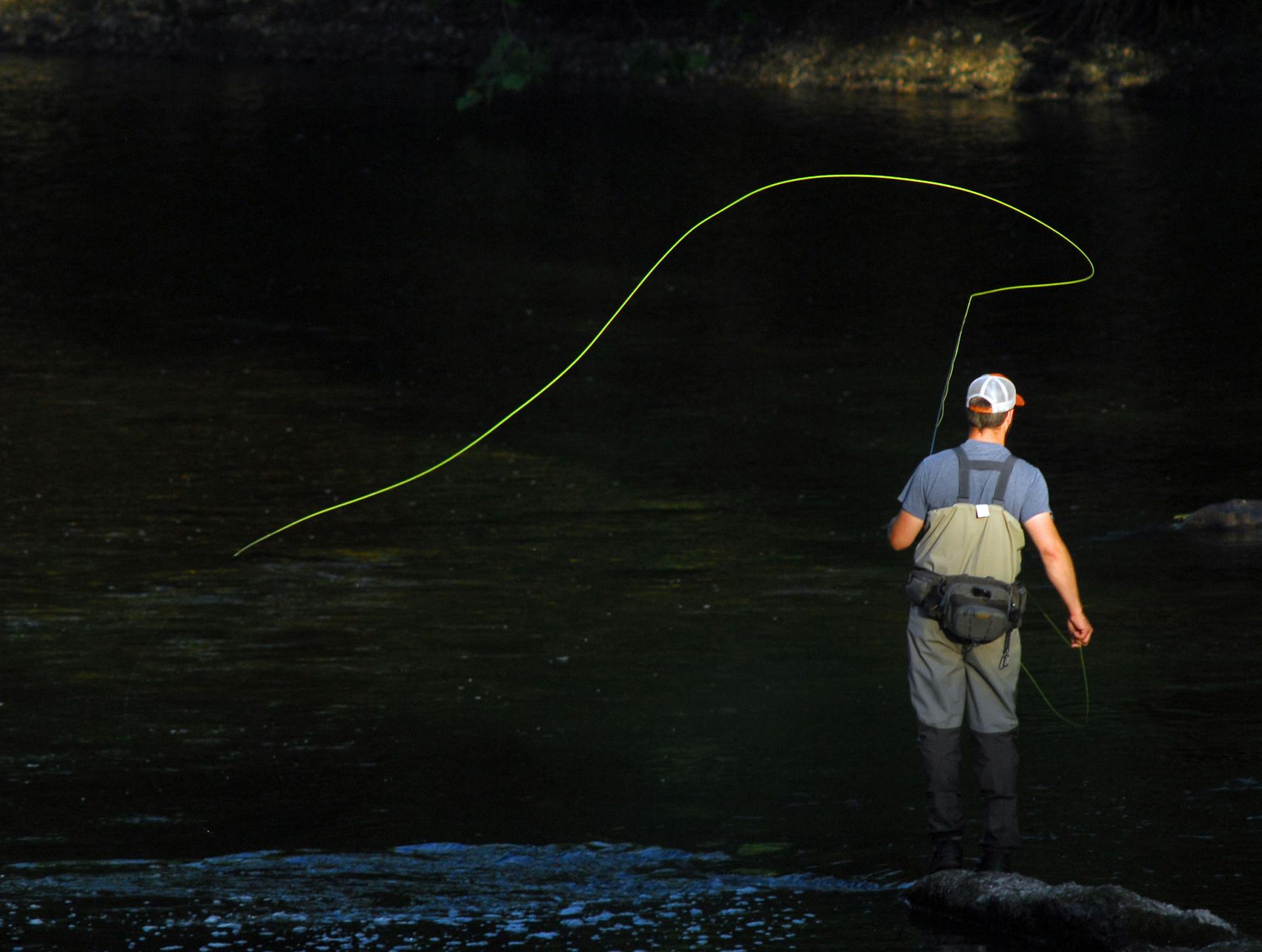 A man fly fishing in a river, enjoying leisure time and outdoor recreation.