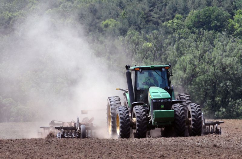A green tractor plowing a field creating clouds of dust