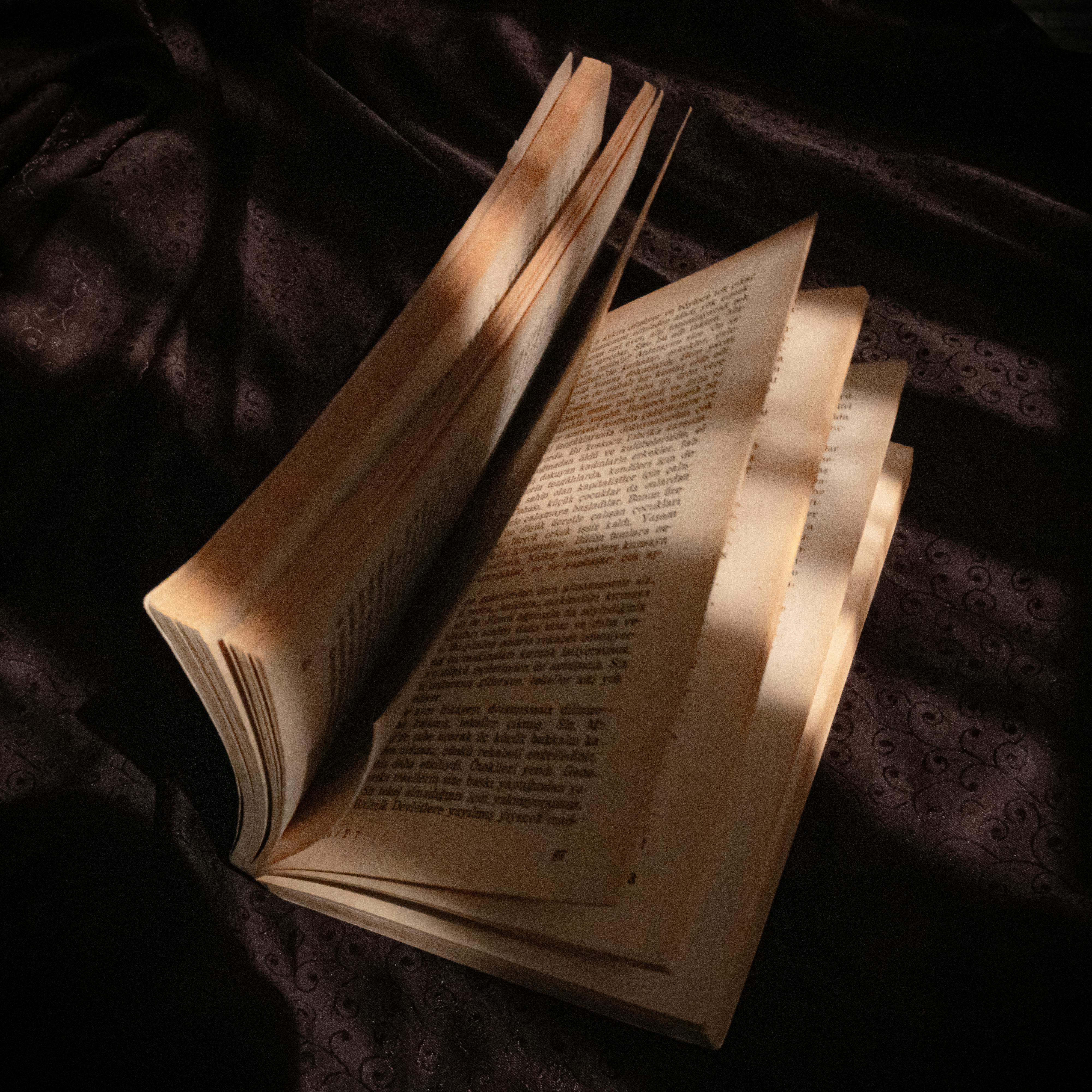 An open vintage book on a dark cloth, showcasing dramatic light and shadow play.