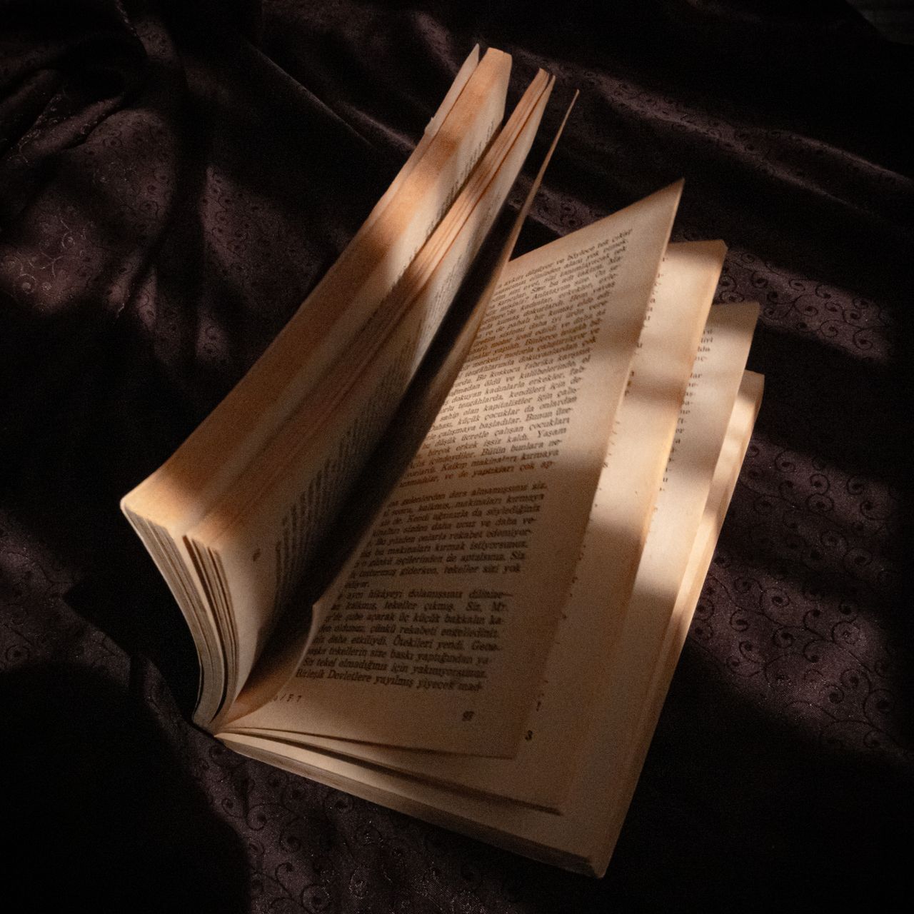 an open vintage book on a dark cloth showcasing dramatic light and sha