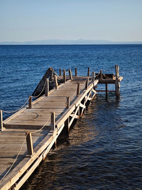 Free Serene view of a wooden pier extending into a calm blue sea under a clear sky. Stock Photo