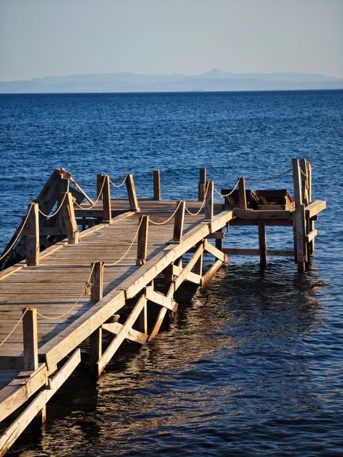 Free A quiet wooden pier extends over a calm blue ocean, offering a peaceful seascape view. Stock Photo