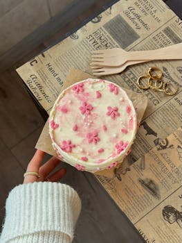 Top view of homemade cake with pink flowers and rustic decor.