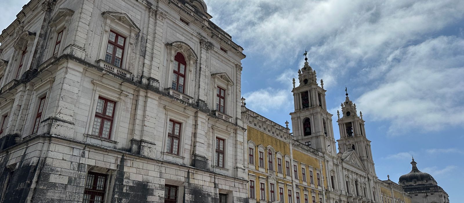 View of the historic Mafra National Palace's intricate facade under a vibrant sky.