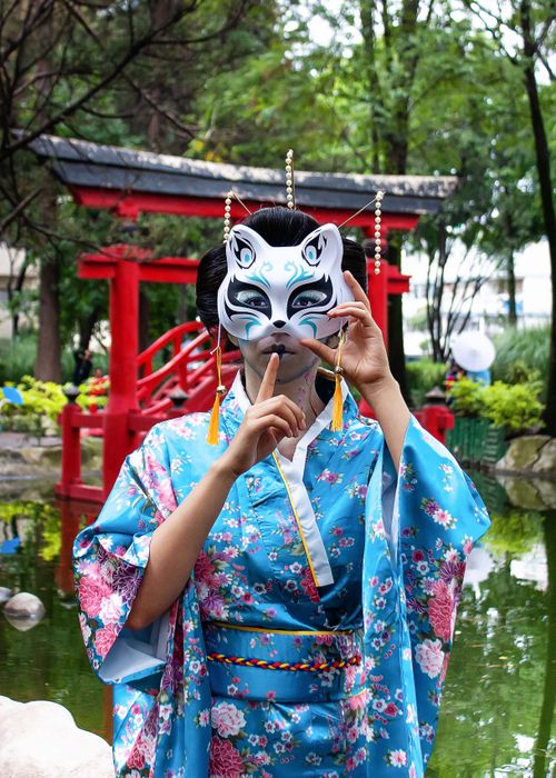 Free A woman poses with a traditional fox mask in a vibrant Japanese garden, wearing a colorful kimono. Stock Photo