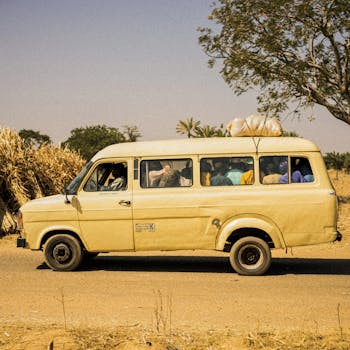 A classic yellow minibus travels on a rural road in Nigeria, carrying passengers and goods.