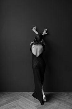 Black and white portrait of an elegant woman in a backless dress posing against a wall.