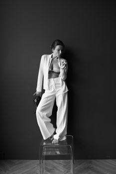 Black and white portrait of an elegant woman in stylish attire standing indoors.