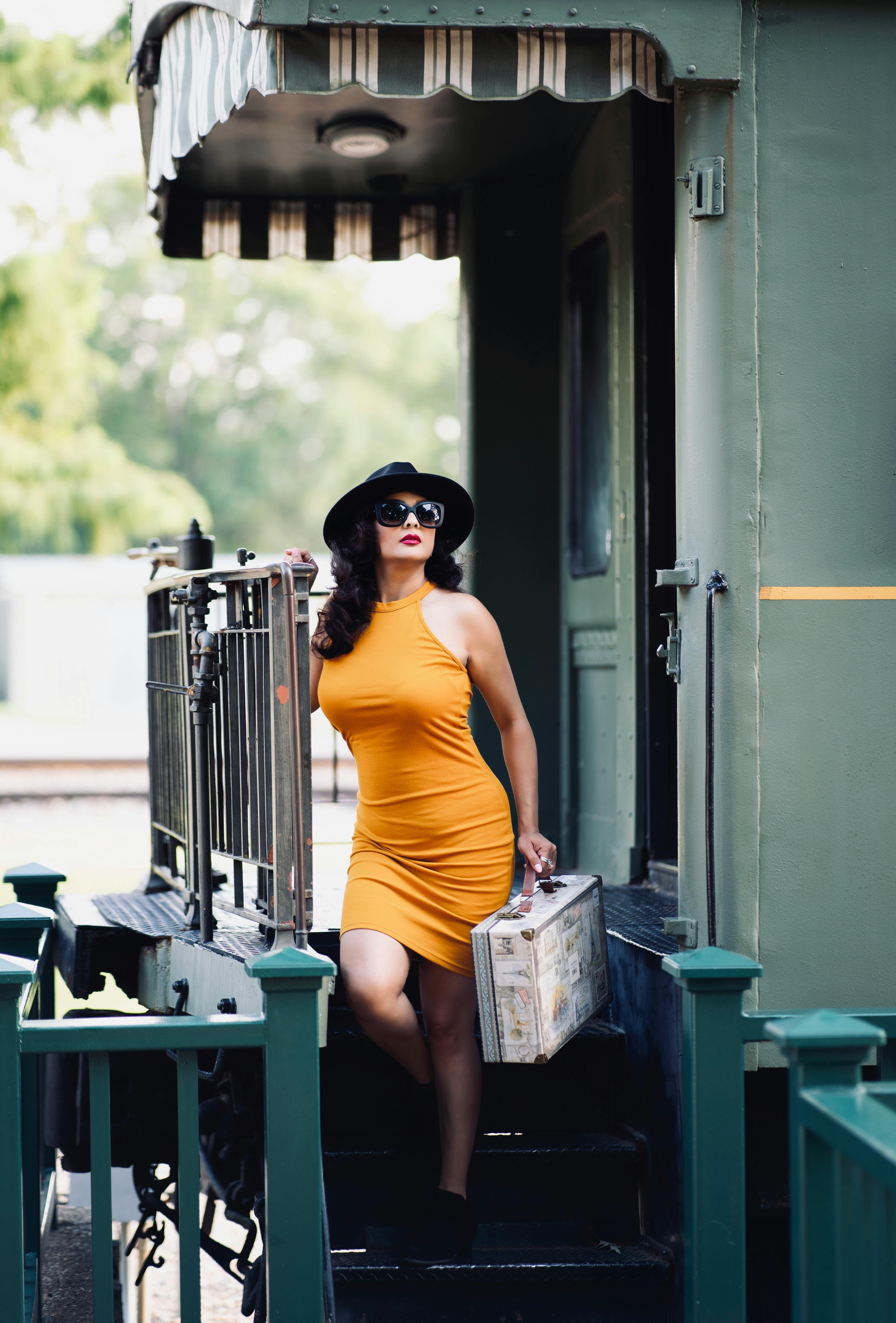 Stylish woman in a yellow dress with luggage on a vintage train carriage, perfect for travel themes.