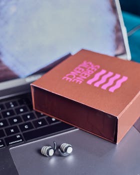 A pair of modern wireless earbuds placed on a laptop beside a chic packaging box.