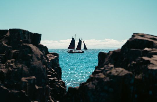 A sailboat glides on turquoise waters framed by rocky cliffs under a clear sky.