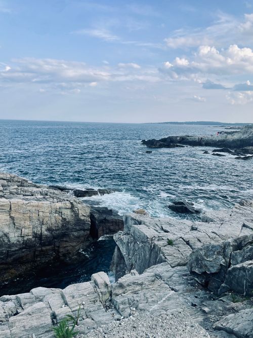 Free A rocky seashore with waves crashing under a clear blue sky, perfect for summer travel vibes. Stock Photo