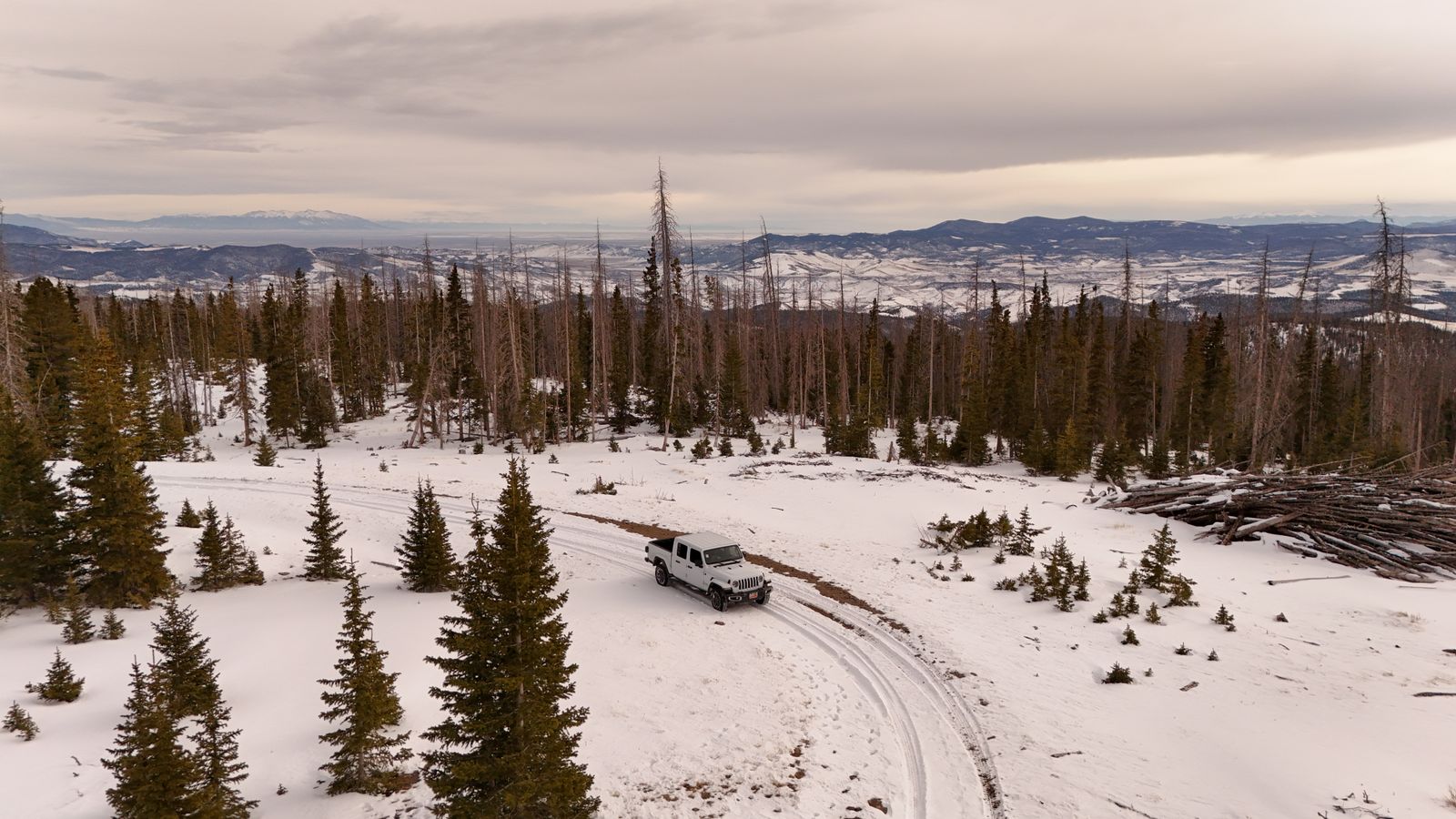 Jeep navigating a snowy mountain trail in Colorado wilderness surrounded by pines and alpine peaks