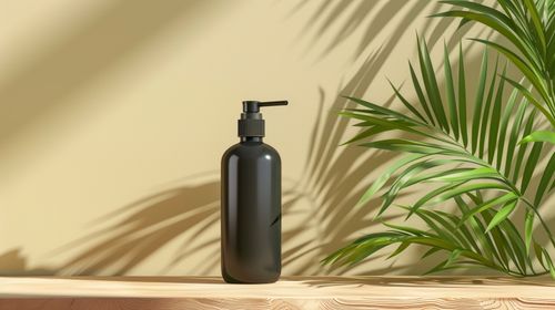 Free A black pump bottle on a wooden surface with tropical leaves casting shadows. Stock Photo