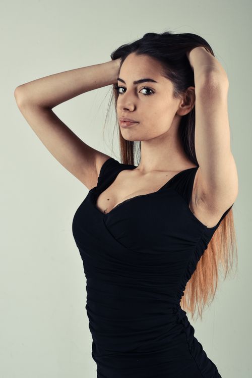 Free Striking portrait of a young woman with long hair in a black dress, posing confidently indoors. Stock Photo