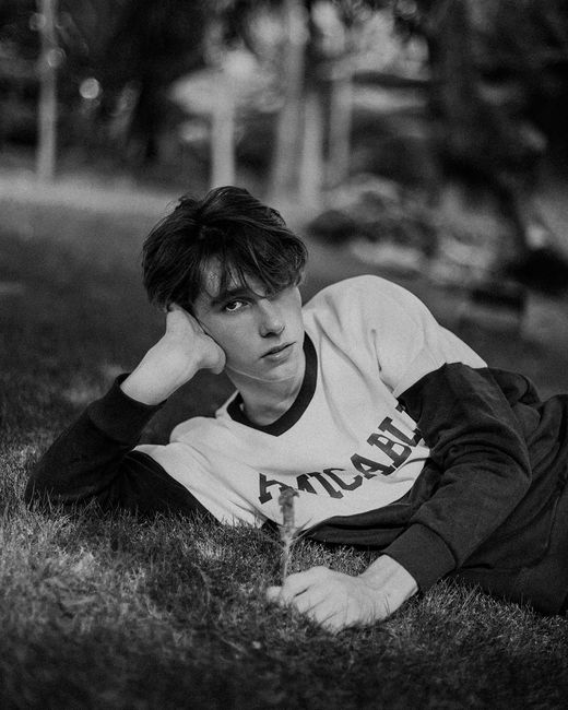 Stylish monochrome portrait of a man lying on grass, modeling a sweater.
