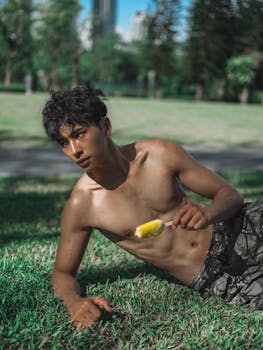 Shirtless young man enjoying a popsicle on a sunny day in the park.