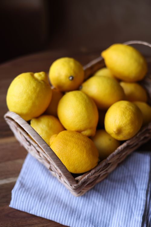 Free A wicker basket filled with bright yellow lemons on a striped cloth, perfect for a rustic kitchen setting. Stock Photo