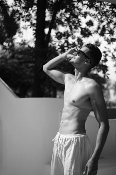 Monochromatic photo of a shirtless man outdoors, wearing sunglasses, embodying strength and style.