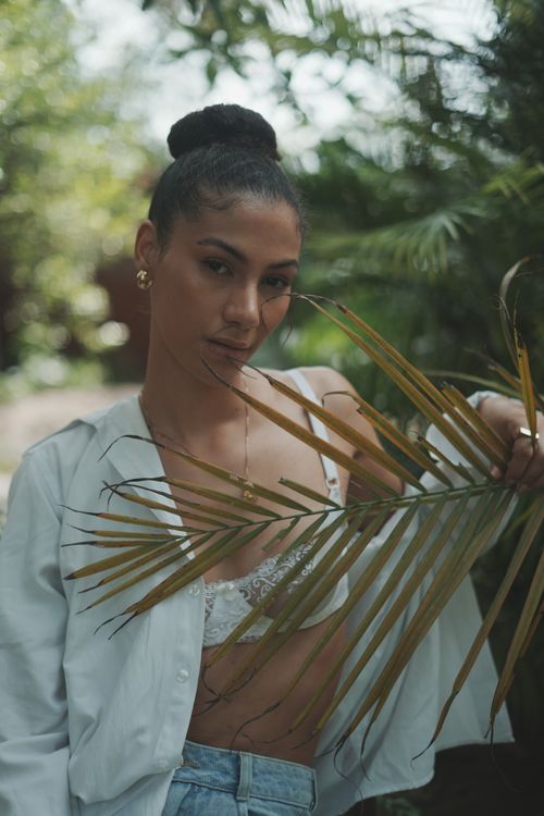 Free Young woman in casual attire holding palm leaves, captured in a serene outdoor setting. Stock Photo