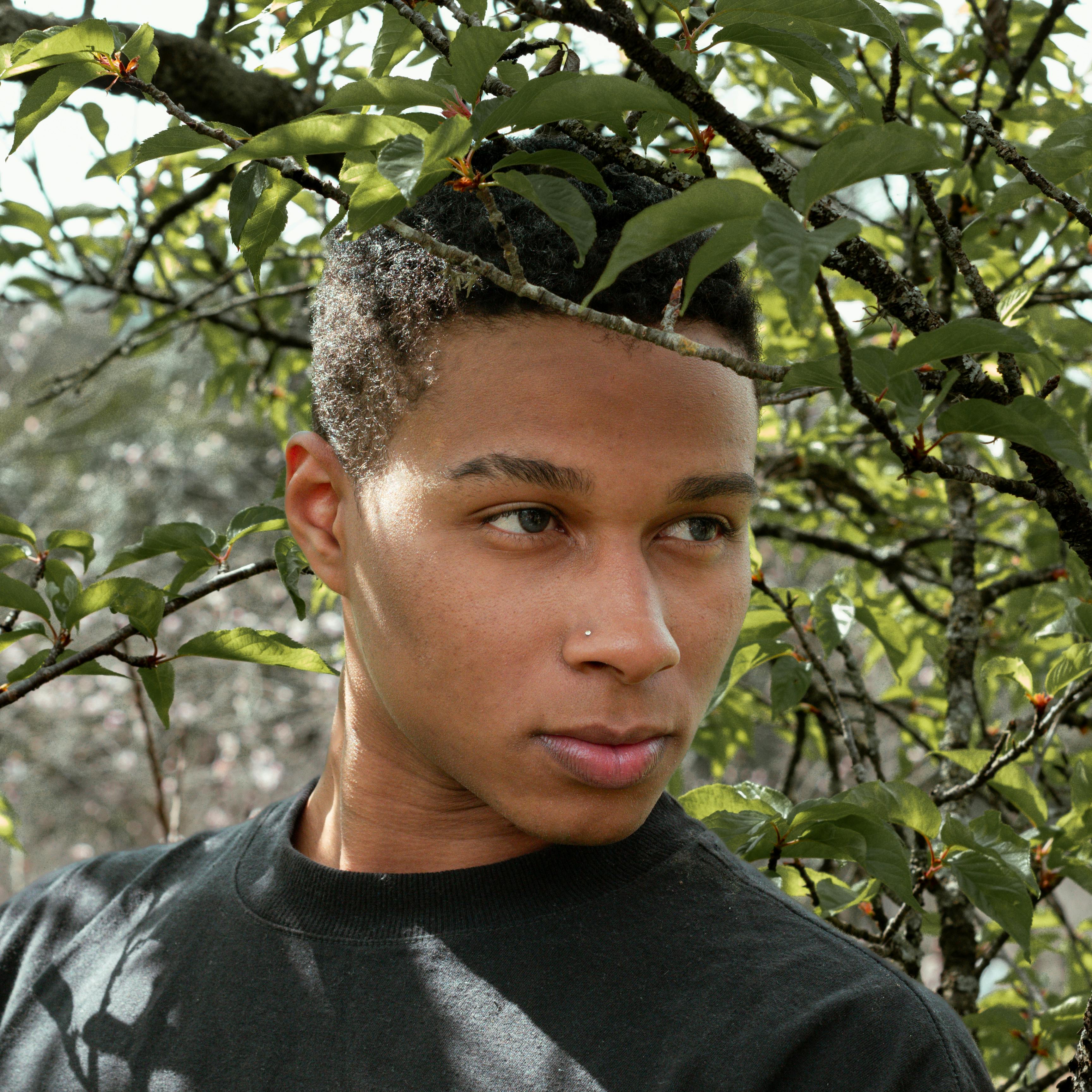 A young man in a black shirt, surrounded by lush green foliage.