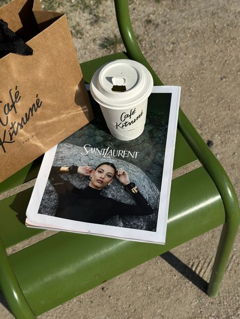 Café Kitsuné coffee and Saint Laurent magazine on a green chair outdoors.