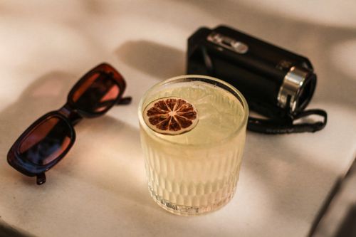Free A glass of lemonade with sunglasses and a vintage camera on a white table. Stock Photo