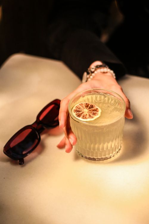 Free Close-up of a hand holding a lemon cocktail with sunglasses on a table, exuding elegance. Stock Photo