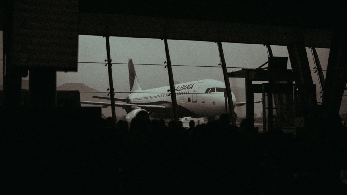 Silhouette of an airplane and waiting passengers inside an airport terminal at dusk.