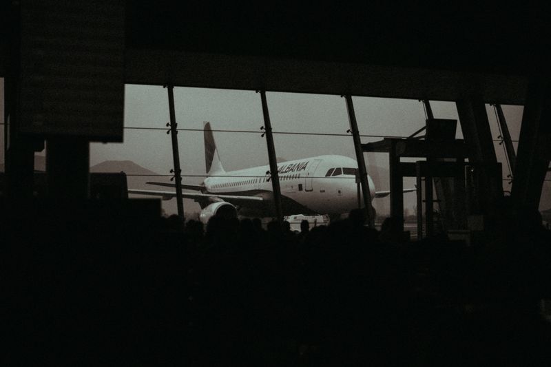 Silhouette of an airplane and waiting passengers inside an airport terminal at dusk.