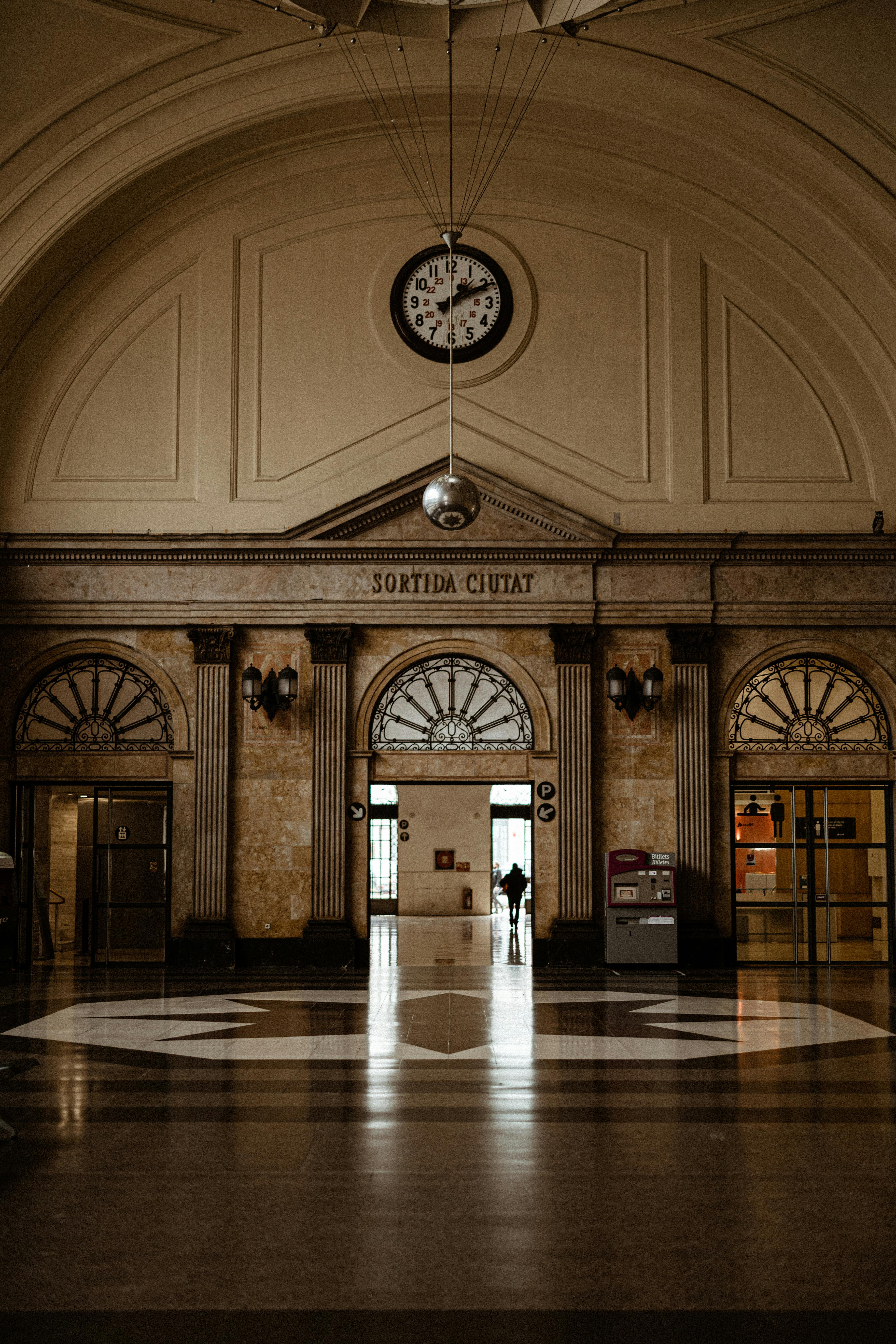 A vintage train station interior featuring a clock, ornate architecture, and an arched ceiling.