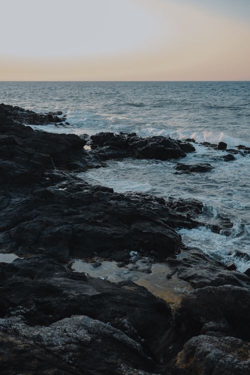 Free A stunning view of a rocky coastline with waves crashing at sunset. Stock Photo