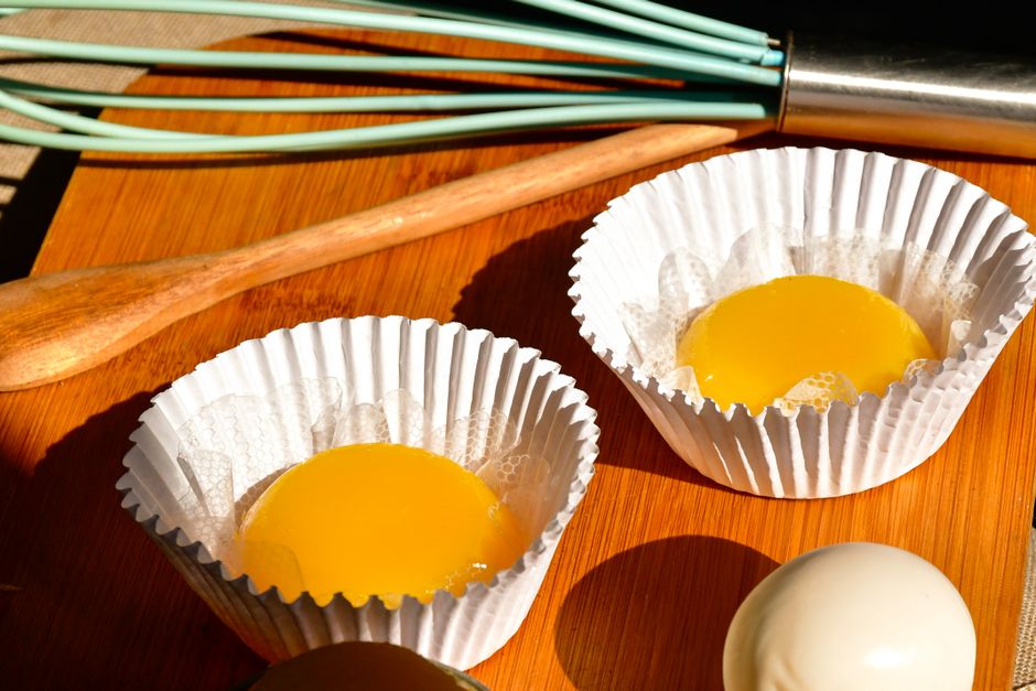 Two egg yolks in paper cups with baking tools on a wooden board, ready for cooking.