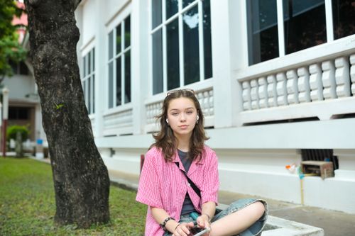 Free A young woman sitting casually outside a building, enjoying a moment of relaxation. Stock Photo