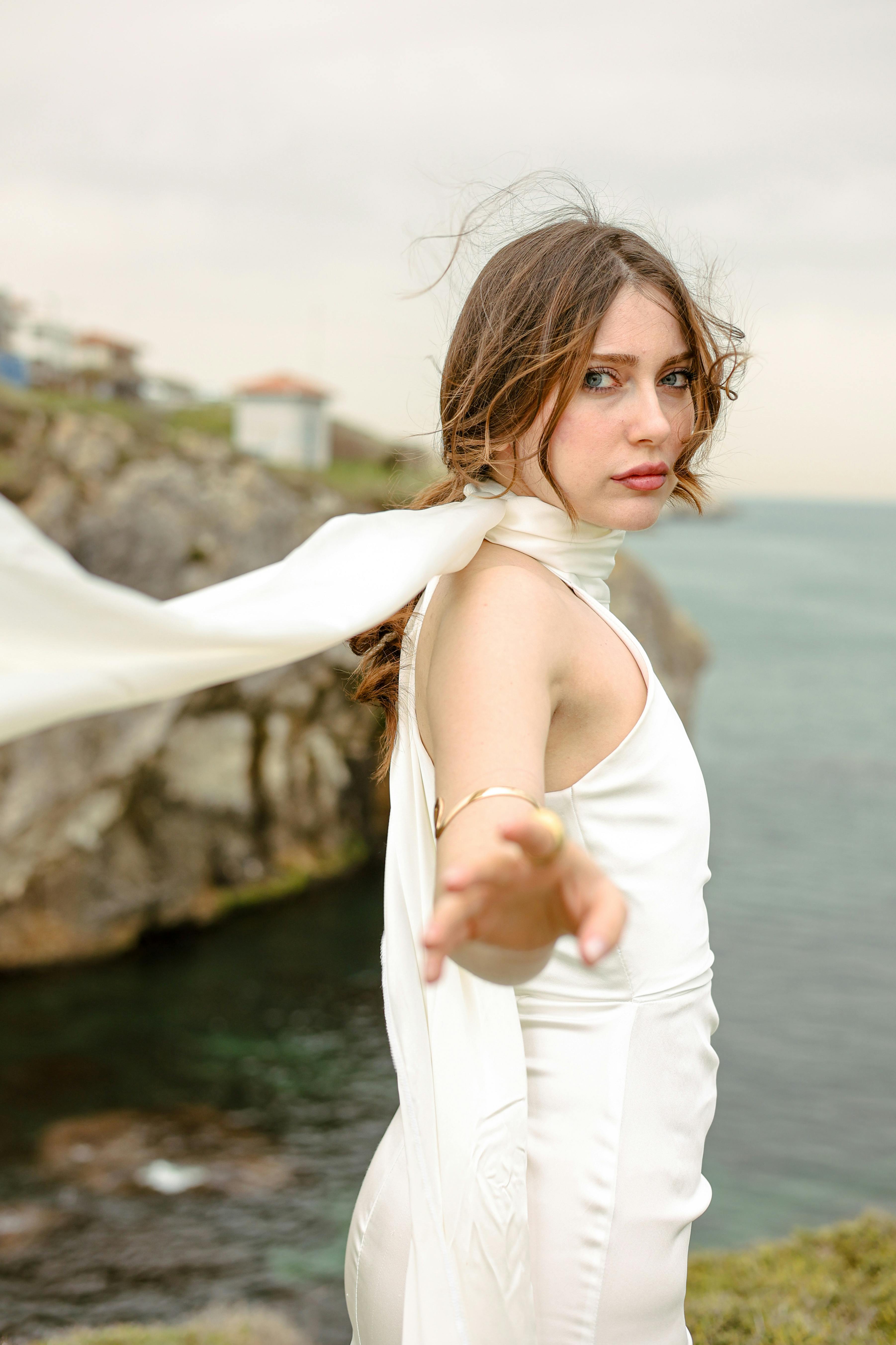 A woman dressed elegantly standing near the sea, exuding grace and freedom.