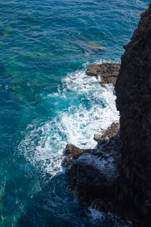 Free Waves crashing against the rugged cliffs of Madeira, Portugal, under the bright summer sun. Stock Photo