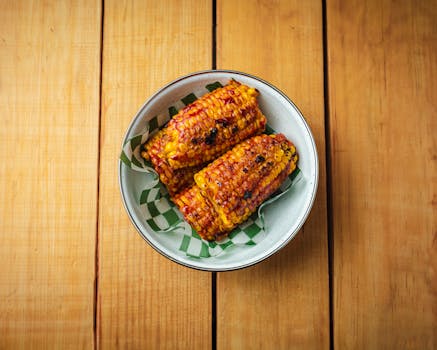 Savor the taste of grilled Mexican elotes drizzled with spicy sauce on a rustic wooden surface.