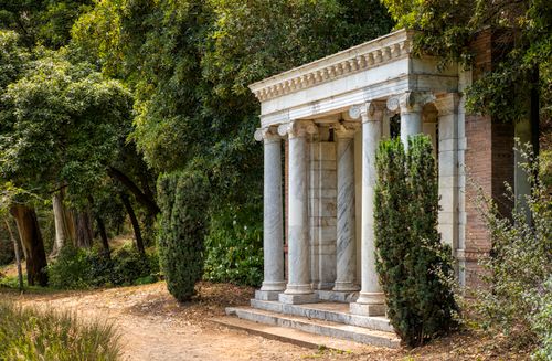 Free Elegant ancient stone building with columns in a verdant garden setting. Stock Photo